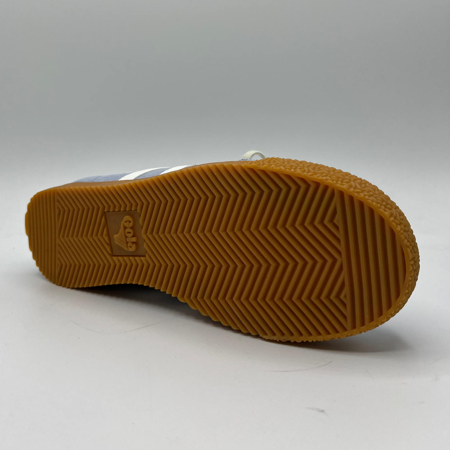 Bottom view of a blue suede sneaker with white accents, a gum outsole and a lace up design.
