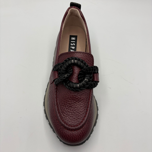 A burgundy pebbled leather loafer with a black braided rope detail across the vamp, photographed from a top-down angle on a white background. The insole features a black label with the brand name 'HISPANITAS’