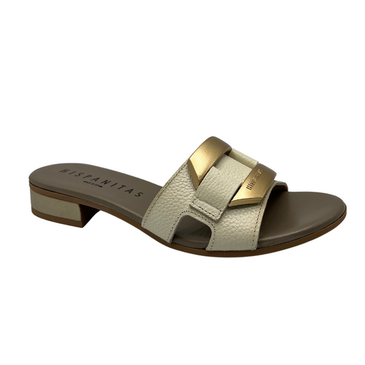 Angled view of slip on sandal with a cream coloured leather strap. Leather lined, short block heel and gold detail on upper.