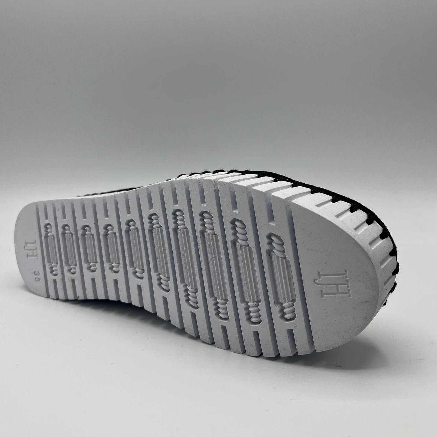 Bottom view of a black and white shoe with elastic panels, a pull on heel tab, and a white rubber outsole.