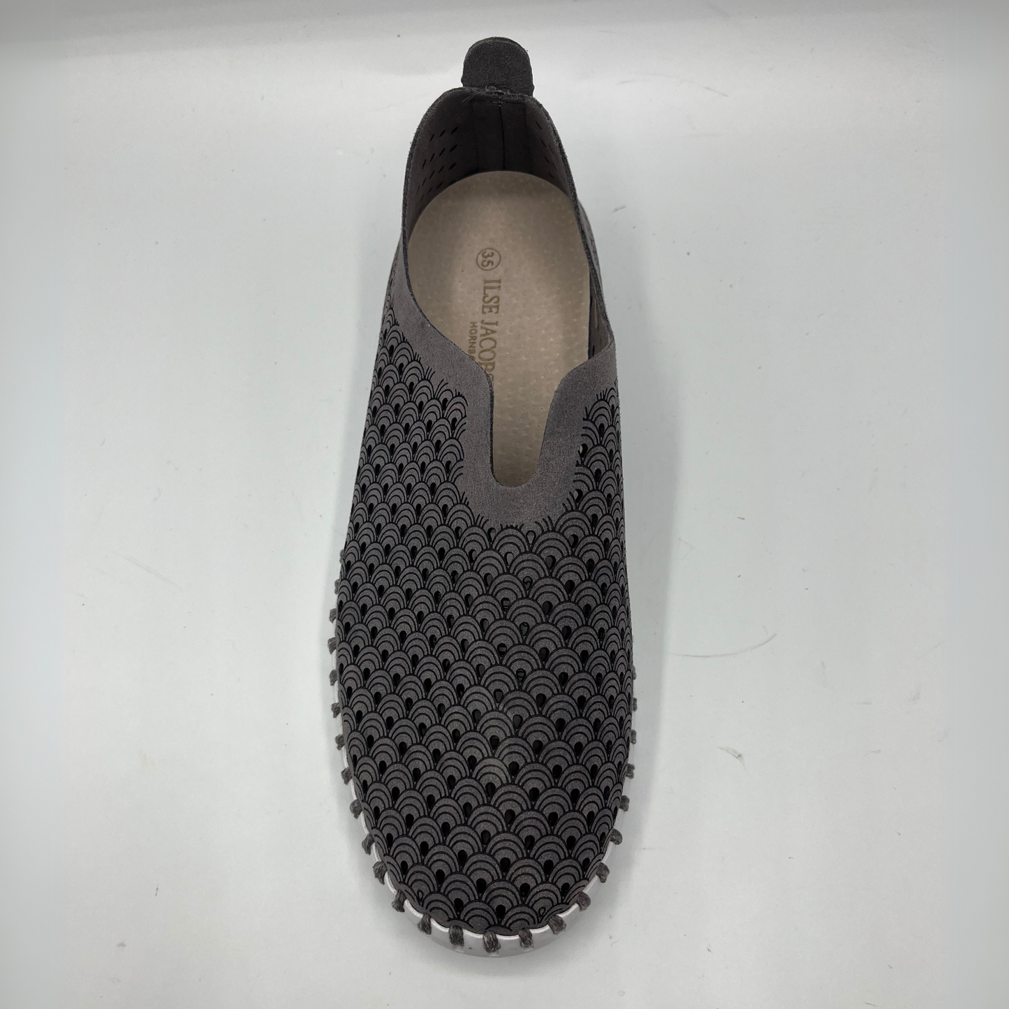 Top view of grey smoked pearl slip on shoe with an intricate laser cut upper and white rubber outsole.