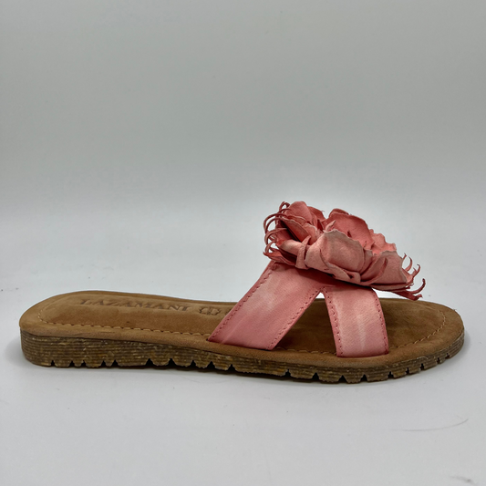 Right facing view of a coral pink slip on sandal with a handmade leather flower detail on the strap and a brown footbed.