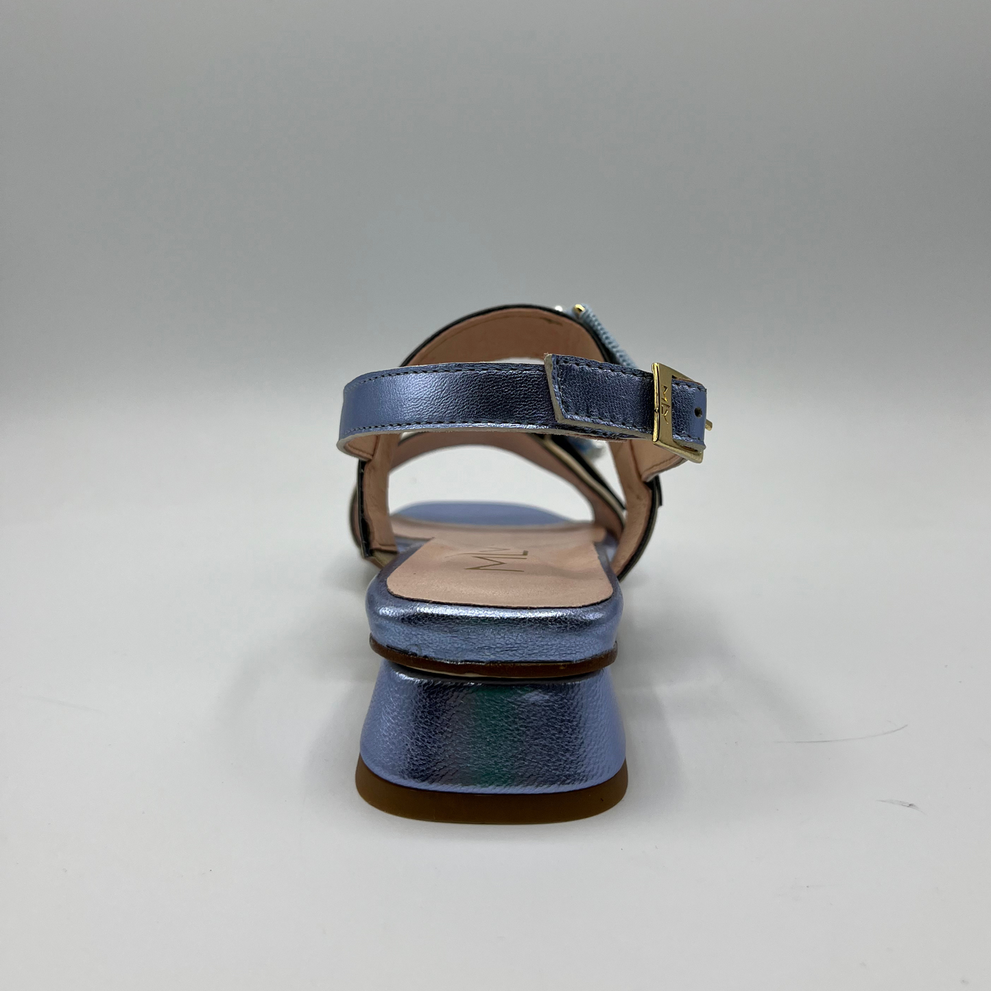 Back view of a blue metallic leather sandal with a leather lining and upper. Large buckle straps and one delicate sling back strap. Low block heel and delicate pearl details on the buckles.