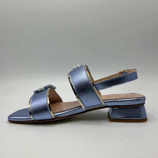 Left facing view of a blue metallic leather sandal with a leather lining and upper. Large buckle straps and one delicate sling back strap. Low block heel and delicate pearl details on the buckles.