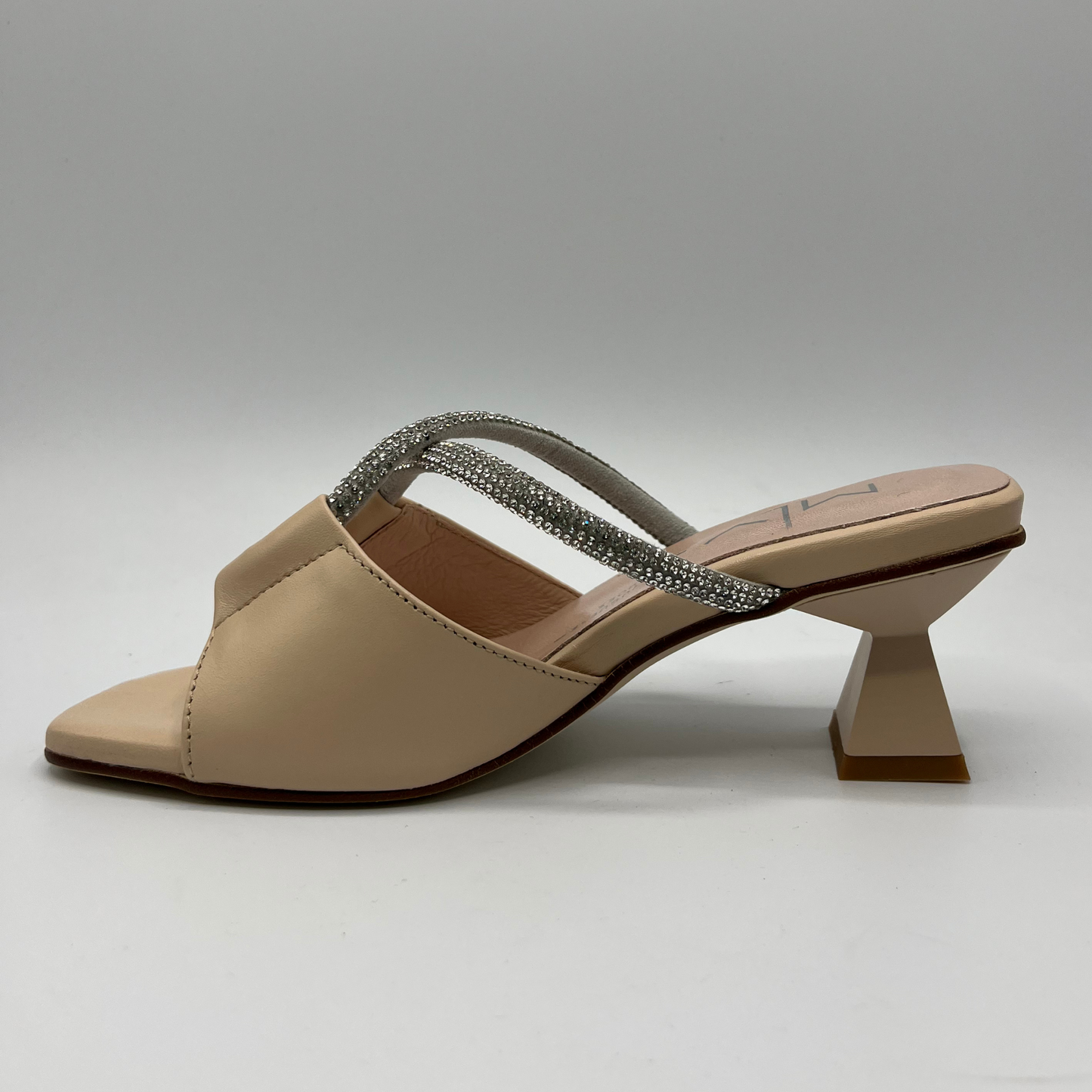 Left facing view of a beige leather sandal with a geometric flared heel, leather lining and a silver jewelled rope detail.