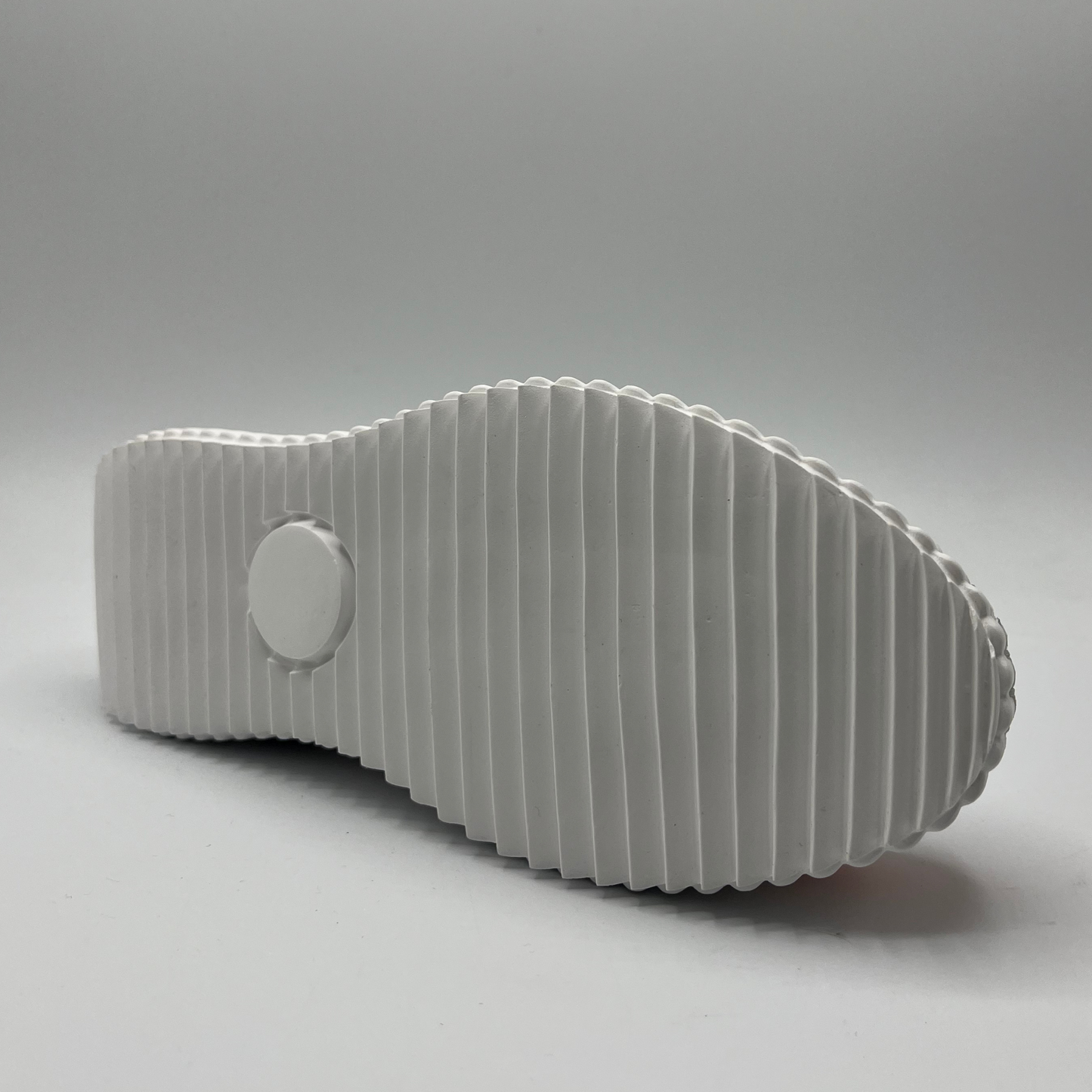 Bottom view of a slip on leather and textile sneaker with stitched details and a white rubber outsole.