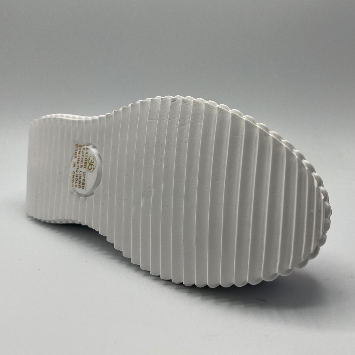 Bottom view of a leather sneaker with side cut outs and a rigid white platform outsole.