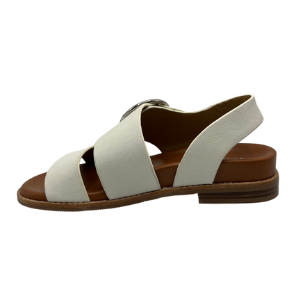 Left facing view of white leather strapped sandals with tan leather lining. Large round silver buckle and low heel
