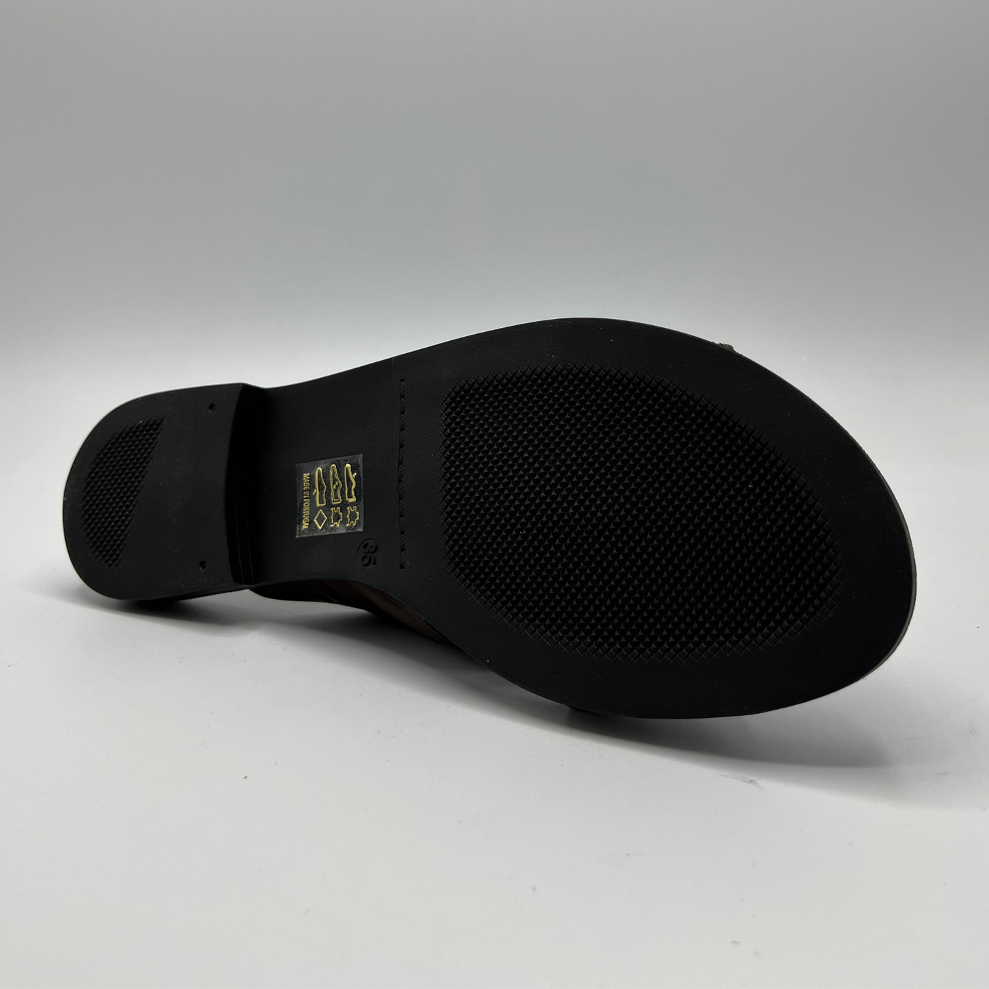 Bottom view of a brown leather slip on sandal with a cross strap design and low heeled outsole. Featuring a silver metal accent on the strap and a cushioned leather insole.