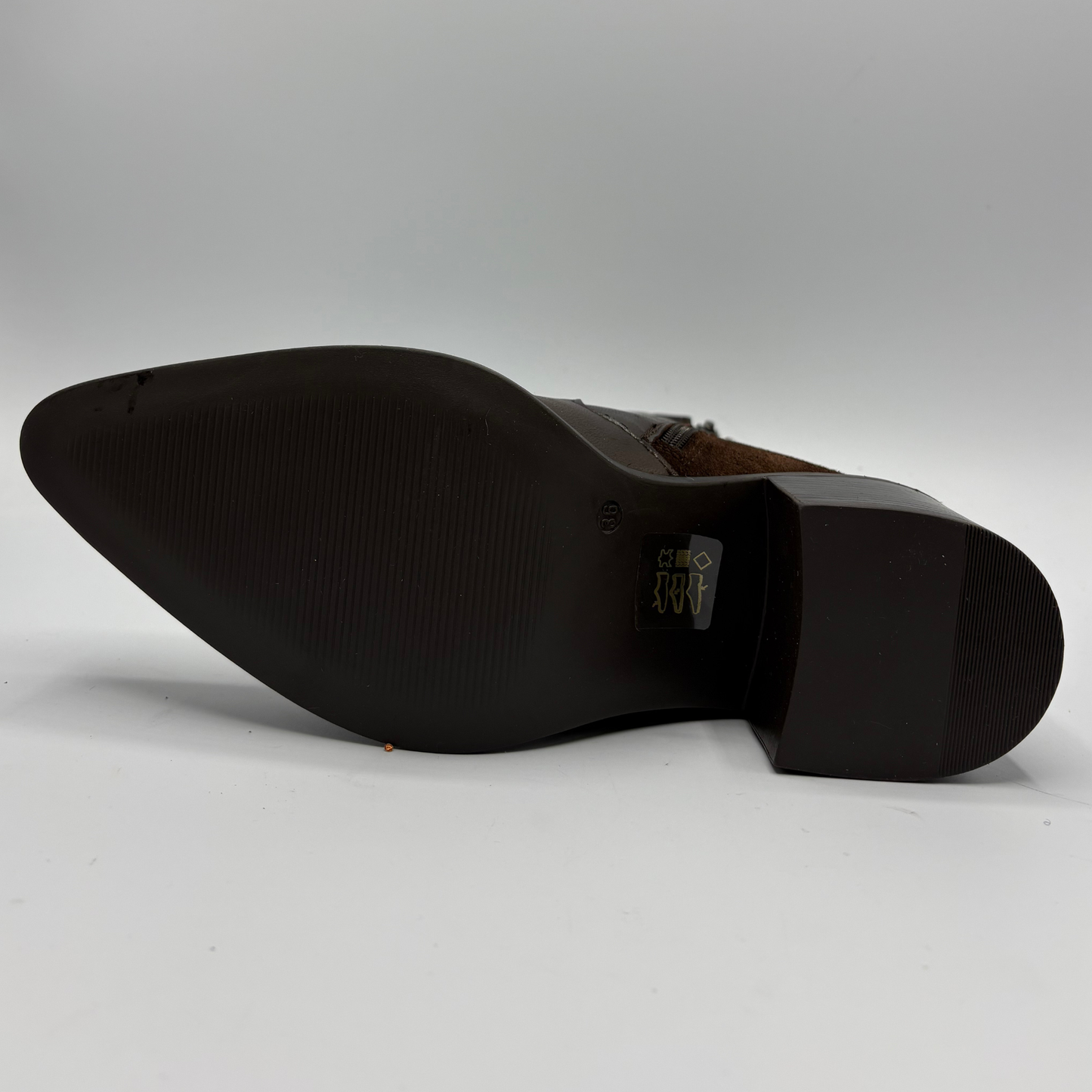 The sole of a dark brown leather boot, showing a pointed toe and a textured black rubber outsole