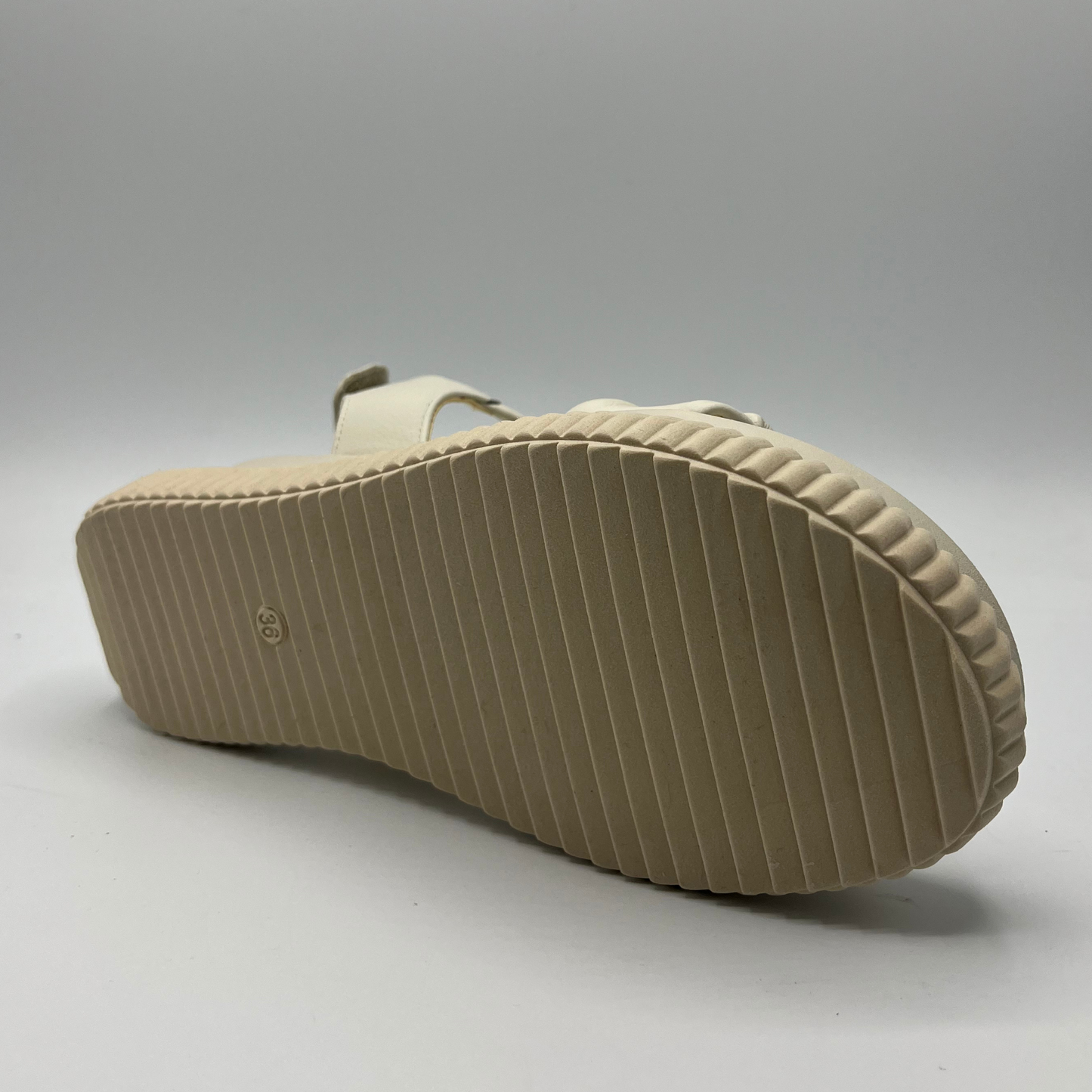 Bottom view of an ivory coloured leather sandal with a thick platform outsole and an adjustable sling back strap.