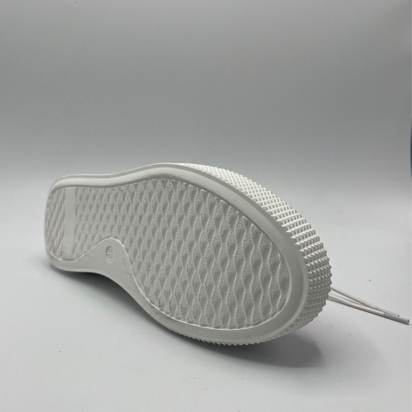 Bottom view of a metallic pink leather sneaker with a thick white rubber outsole and elastic laces.