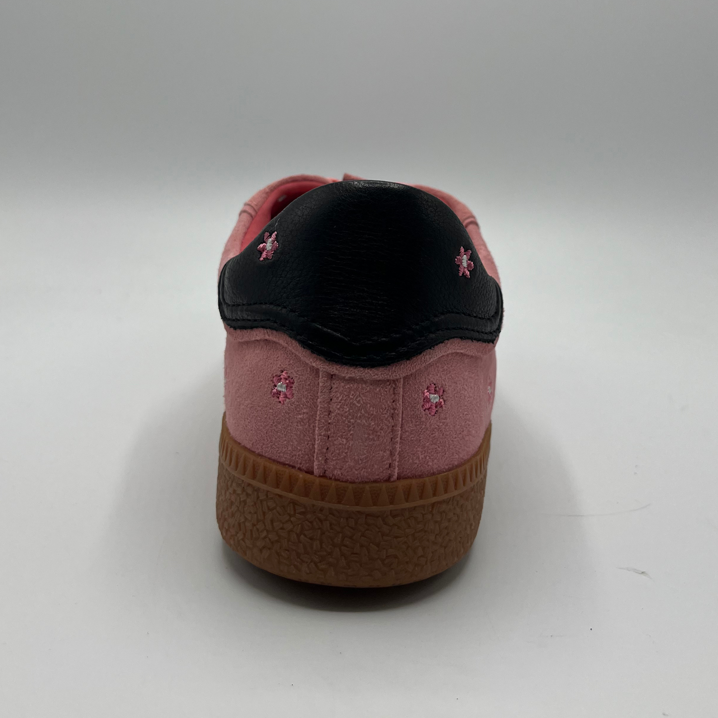 Back view of a pink suede sneaker with a black collar and a tan rubber outsole.