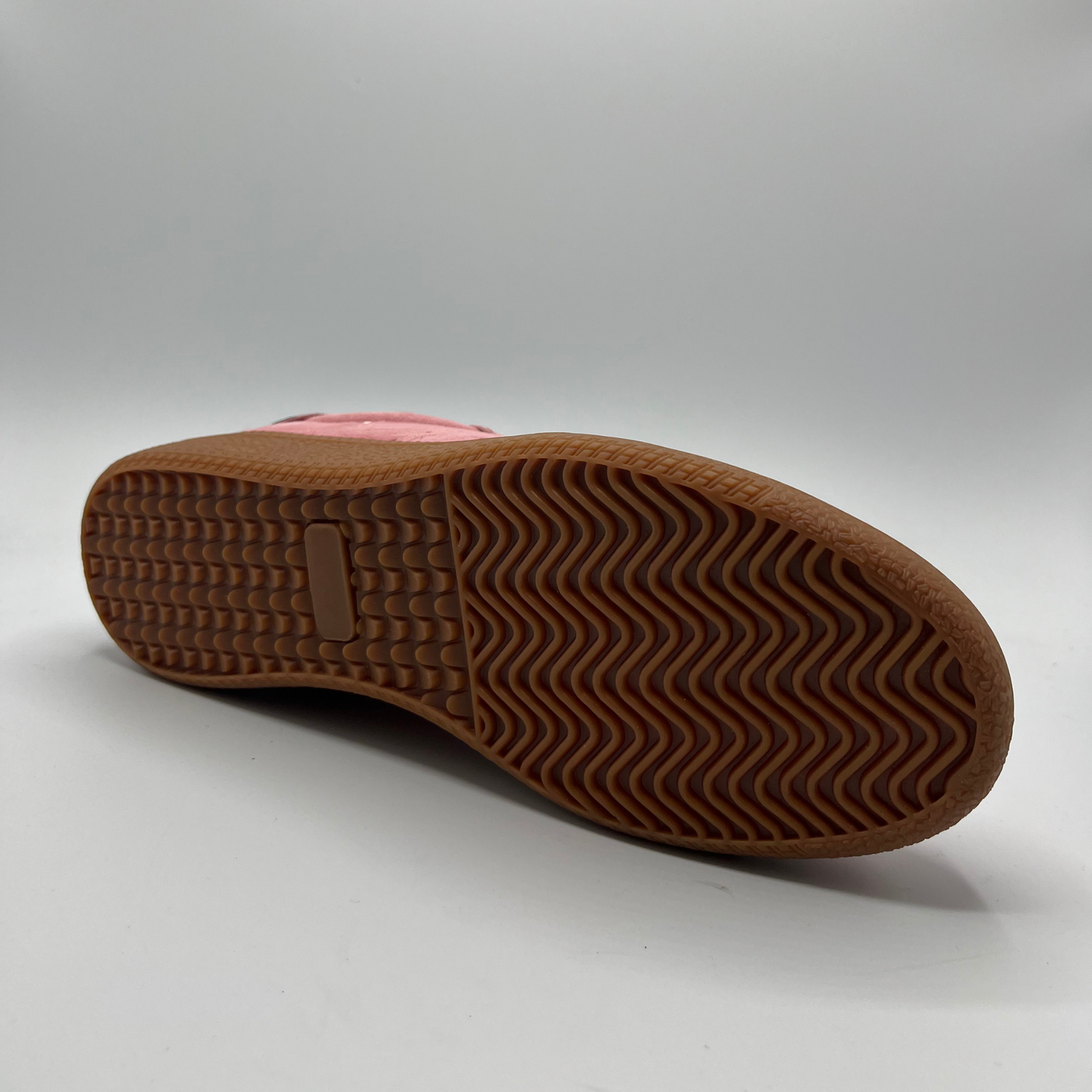 Bottom view of a pink suede sneaker with a black collar and a tan rubber outsole.