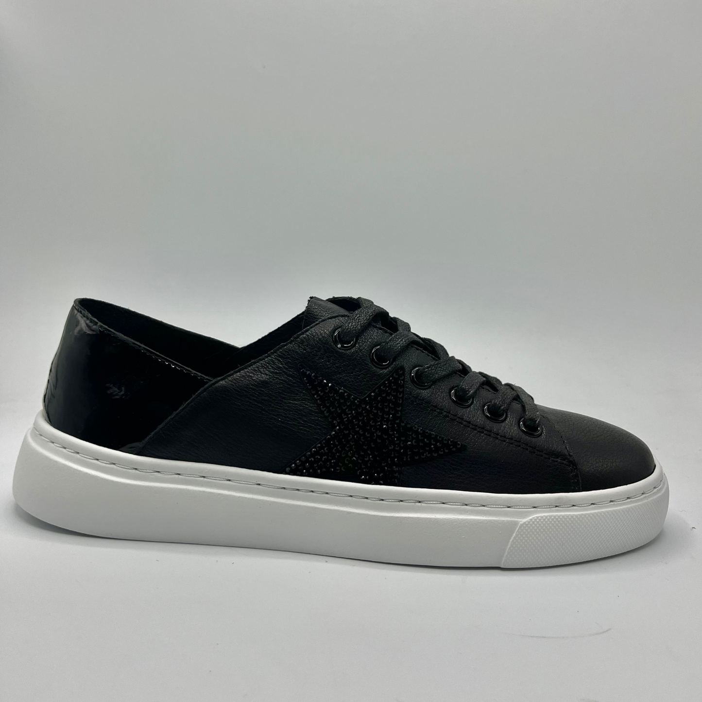 Right facing view of a black leather sneaker with a white rubber outsole and a black jewelled star