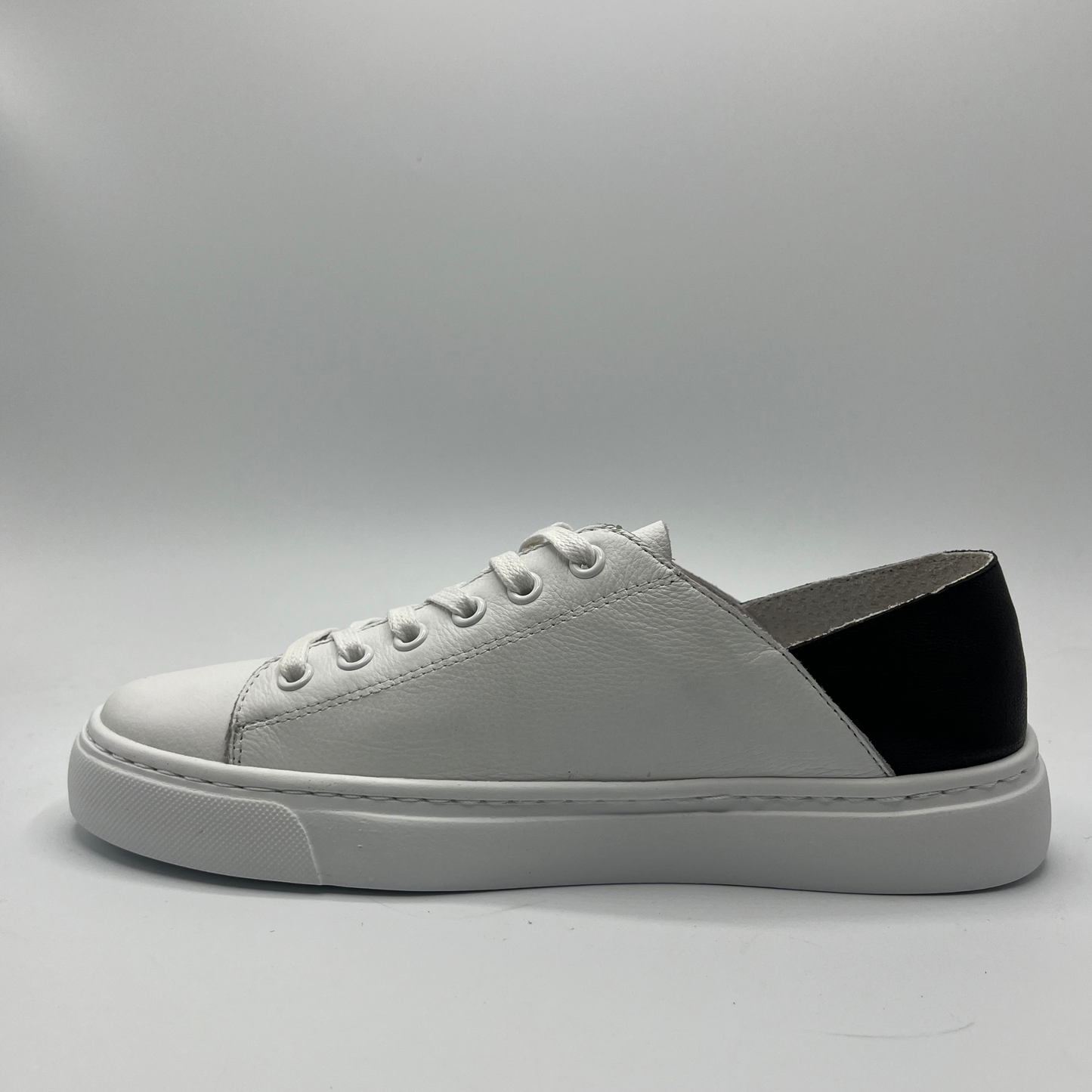 Left facing view of a white leather sneaker with a black heel and white rubber outsole