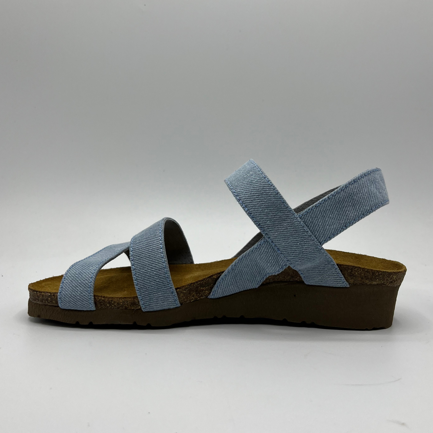 Left facing view of a light denim strapped sandal with adjustable hook and loop and a low wedge heel.