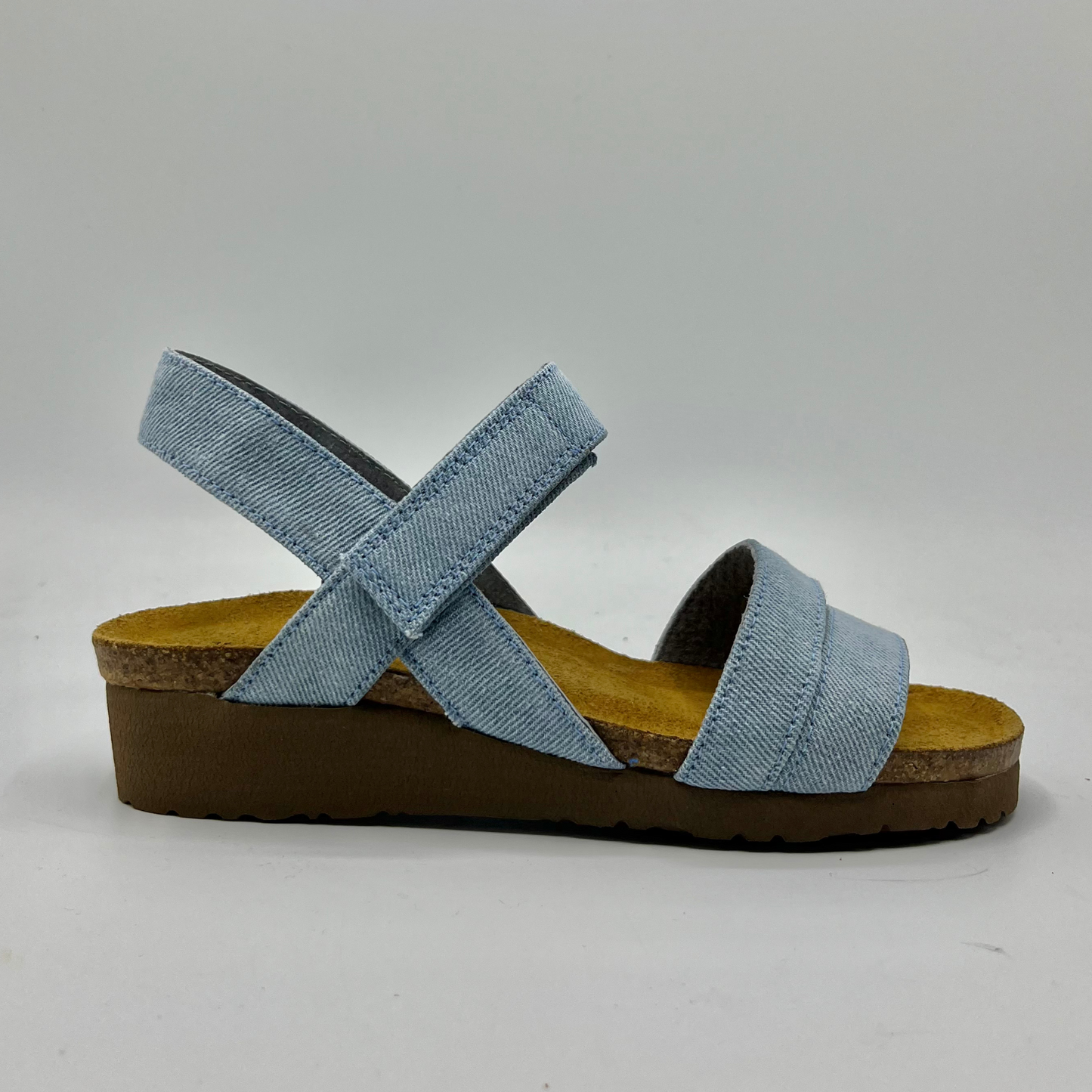 Right facing view of a light denim strapped sandal with adjustable hook and loop and a low wedge heel.