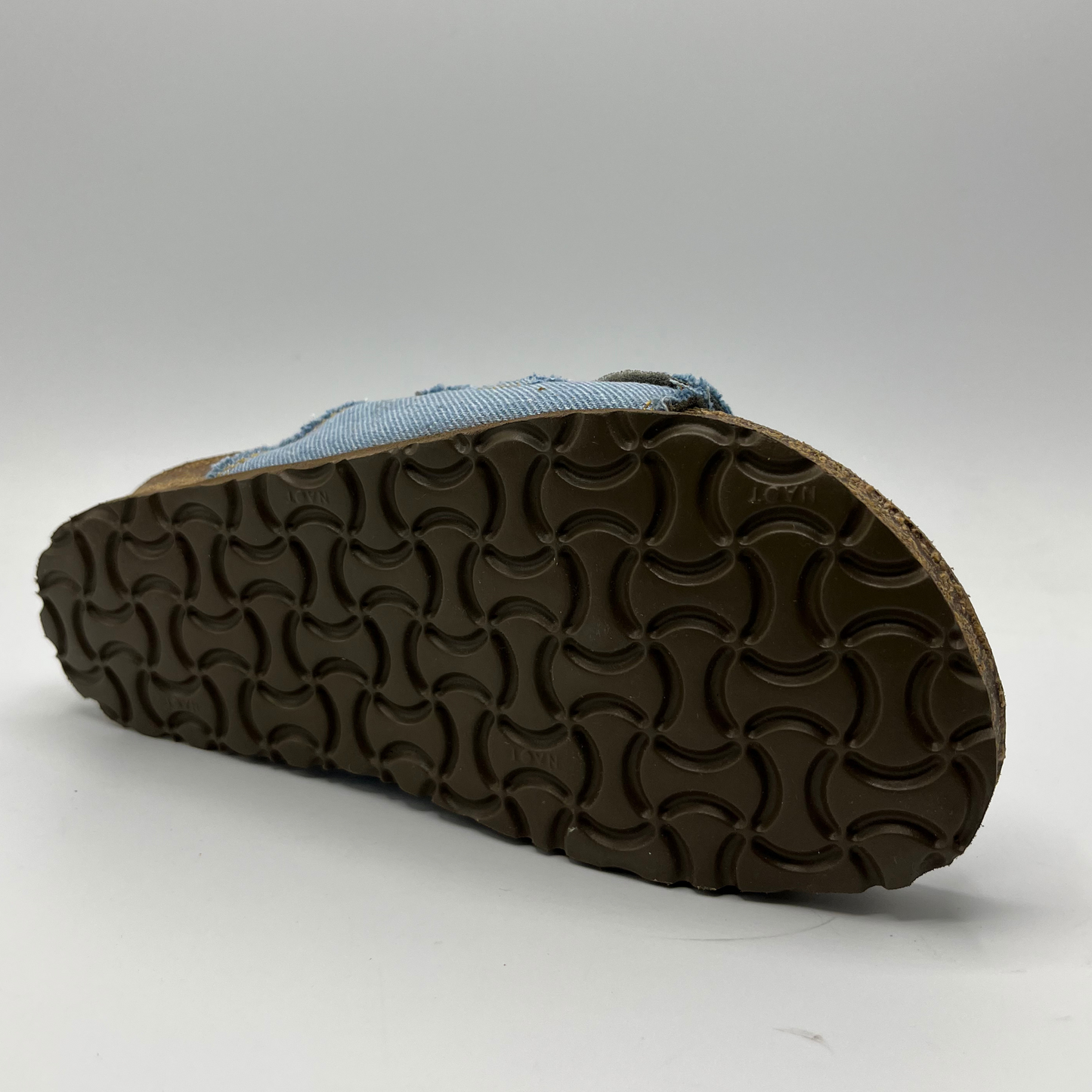 Bottom view of a denim slip on sandal with a contoured cork footbed and two adjustable straps.