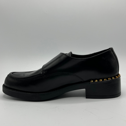 Black loafer shoe with gold studs on a gray background