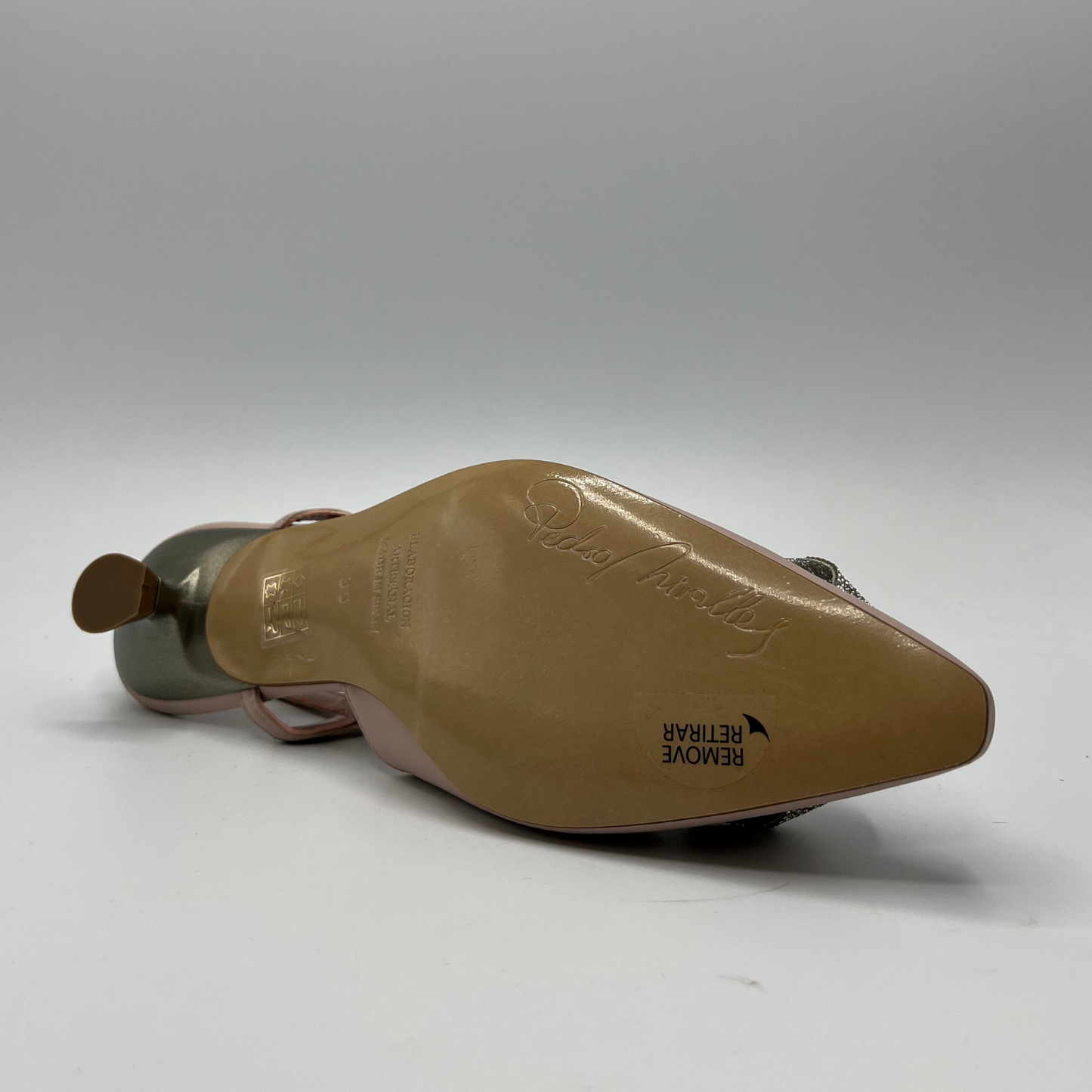 Bottom view of a baby pink leather shoe with a pointed toe, sling back strap, kitten heel and a silver rose detail on the toe.