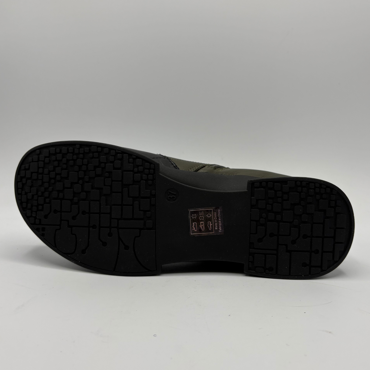 The black rubber outsole of a shoe, showing a textured tread pattern and a small size/manufacturer label in the center, photographed against a neutral gray background.