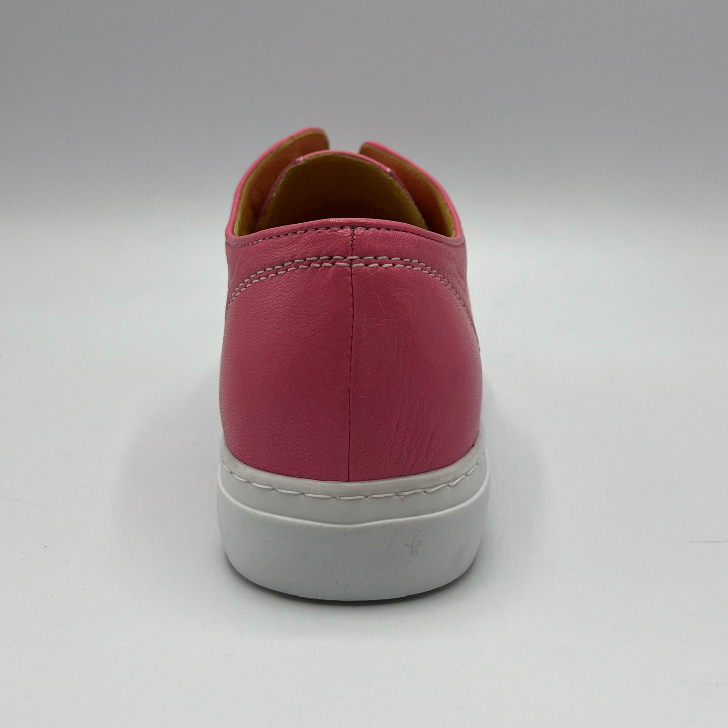 Back view of a fuschia leather sneaker with elastic laces and a white rubber outsole.