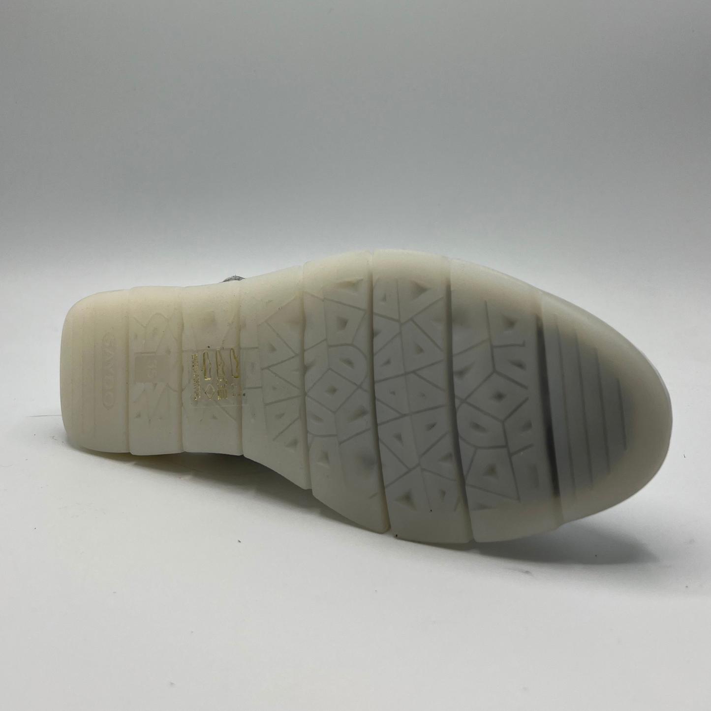 Bottom view of a white leather slip on shoe with a velcro slingback strap and a low wedge heel.