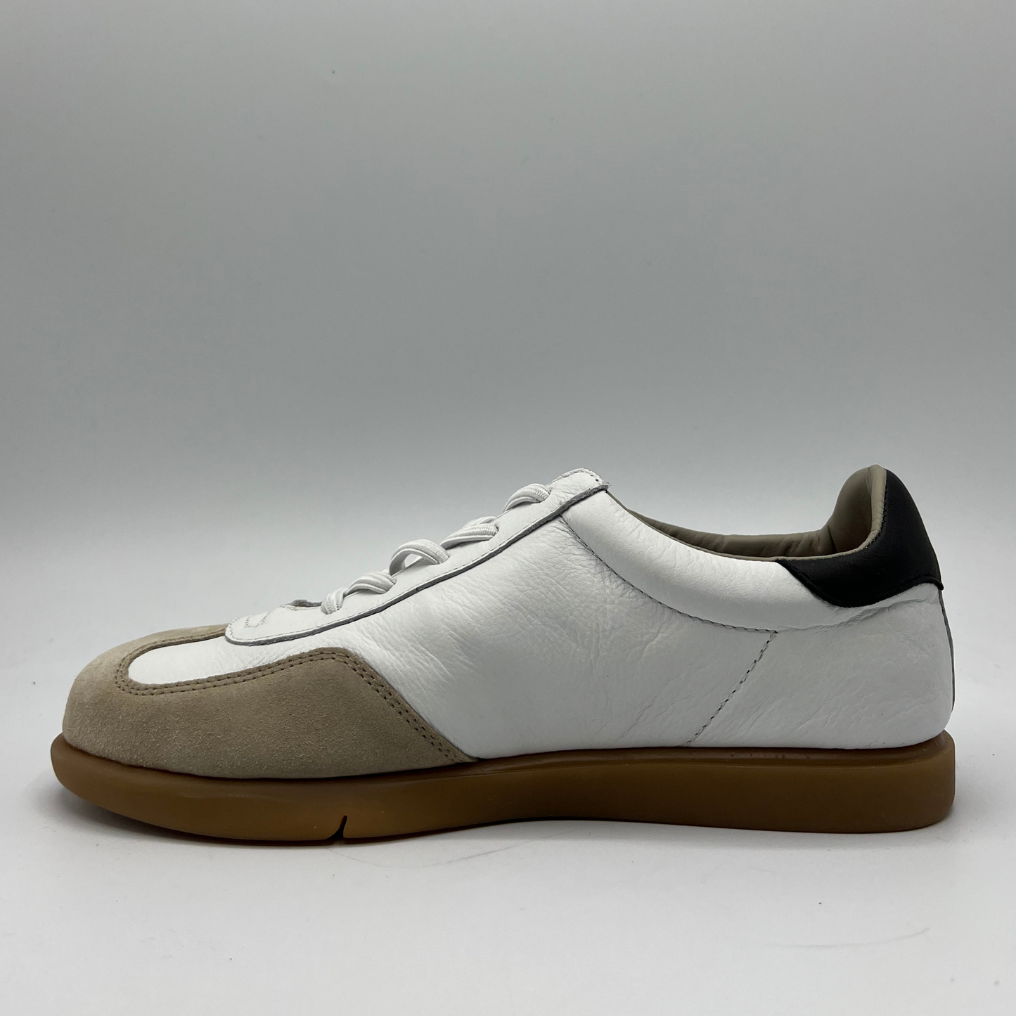 Left facing view of a leather and suede sneaker with a brown rubber outsole and a padded collar.