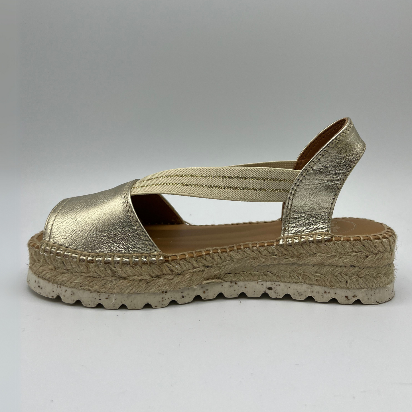 Left view of an espadrille soled sandal with elasticated side straps and platinum leather straps.