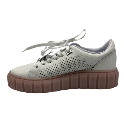 Left facing view of white leather sneakers with rose coloured platform rubber outsole. White laces and perforated leather details on the sides.