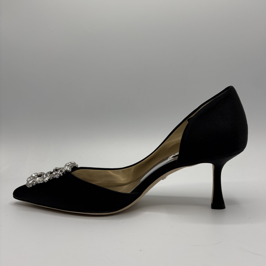 Black high-heeled shoe with a decorative brooch on a gray background