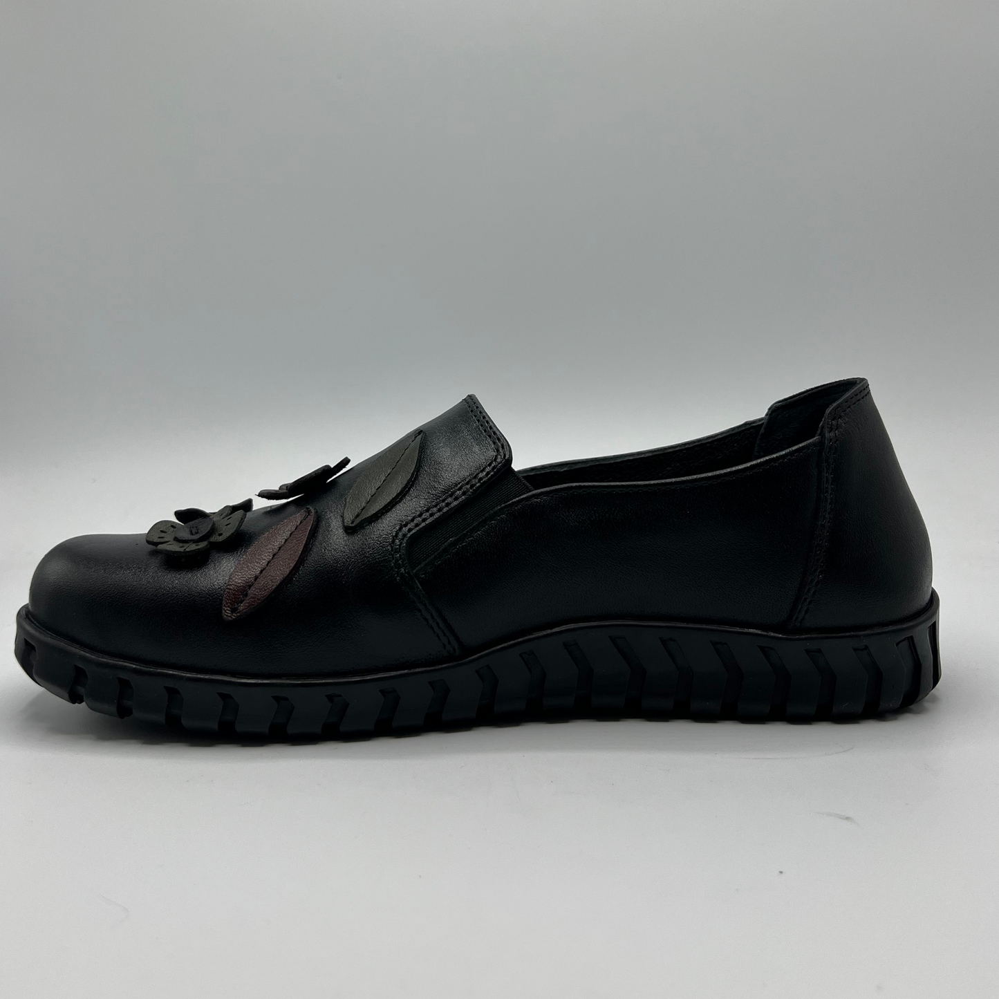 Black slip-on shoe with a decorative element on a gray background
