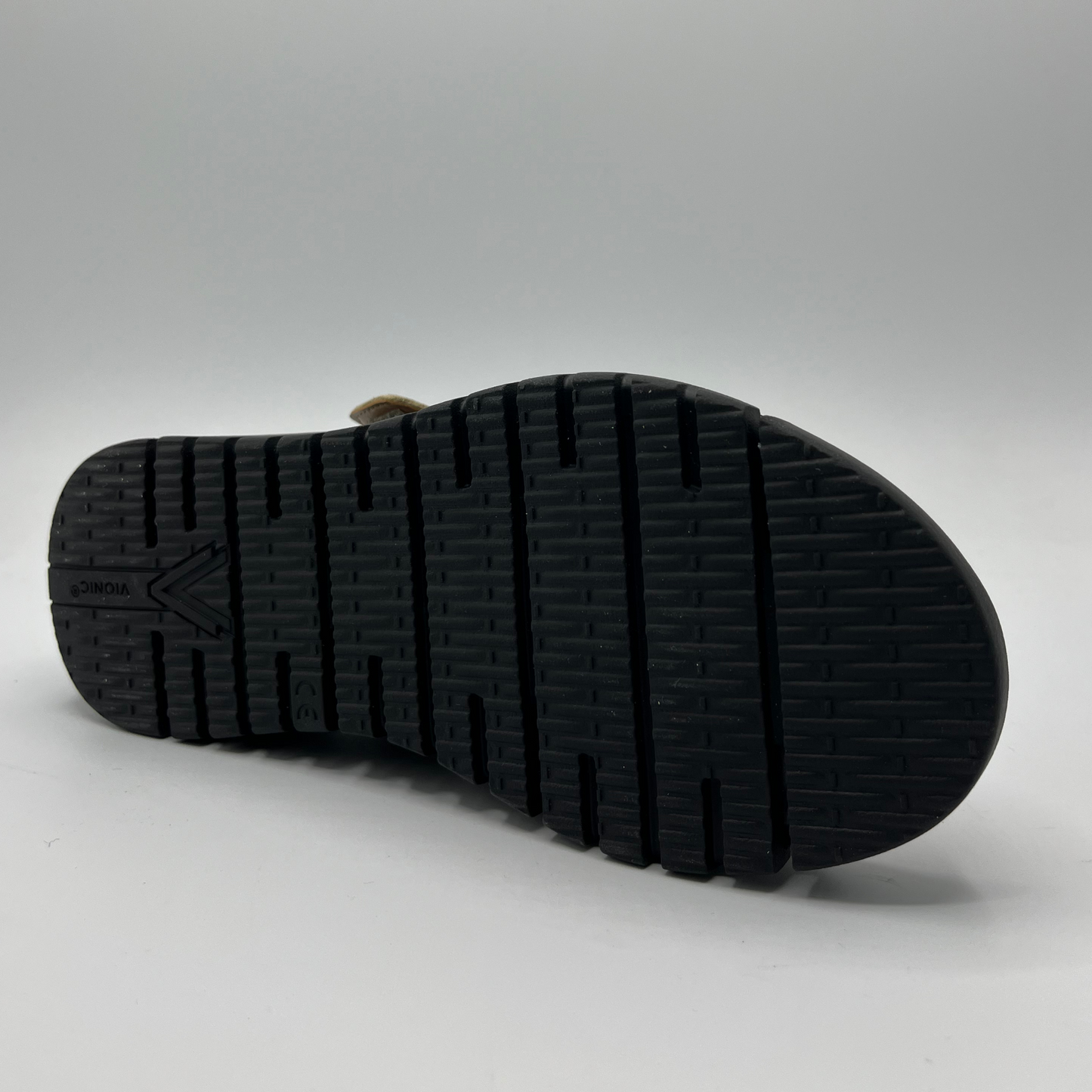 Bottom facing view of a leather strapped sandal with an adjustable hook and loop strap and a black wedge heel.