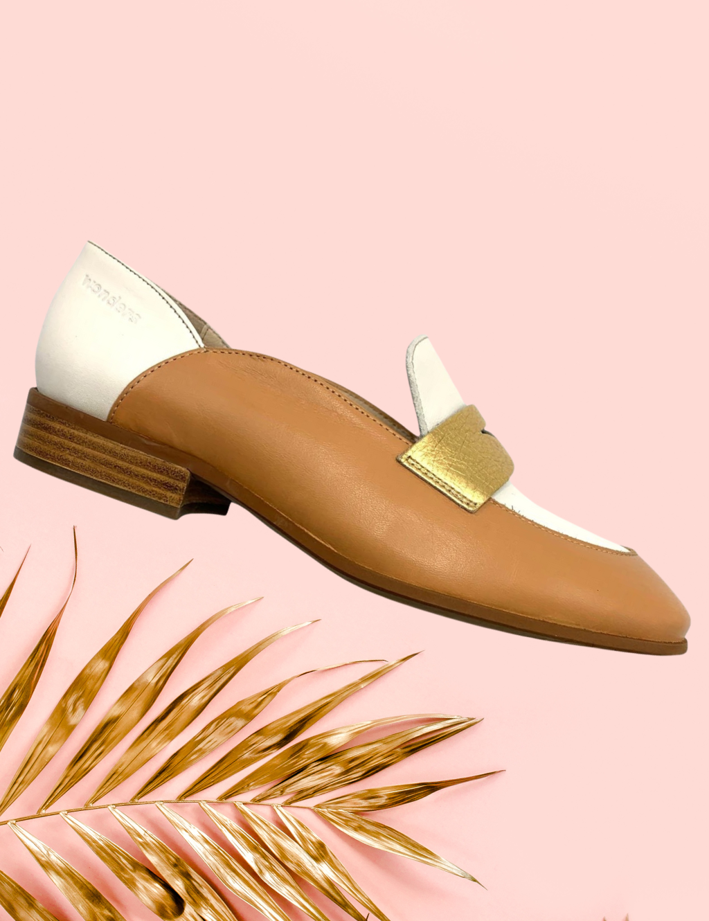 Brown and beige loafer with golden colour strap on pink background with golden coloured palm leaves