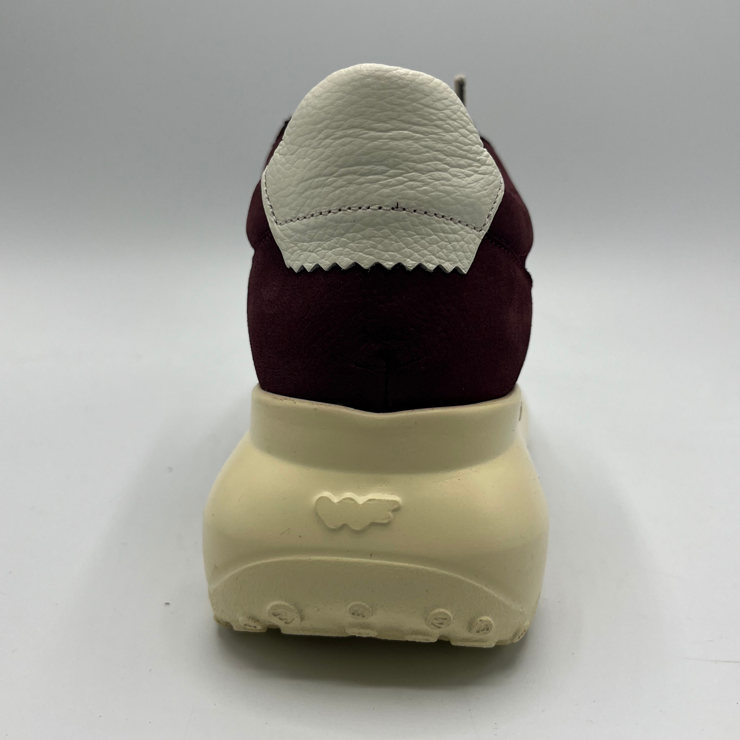 Back view of a sneaker with a maroon sock and beige sole on a gray background