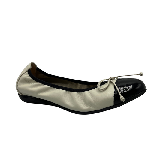 Angled view of off white and black leather ballet flat. It has a Flexible outsole and a delicate bow on the toe.