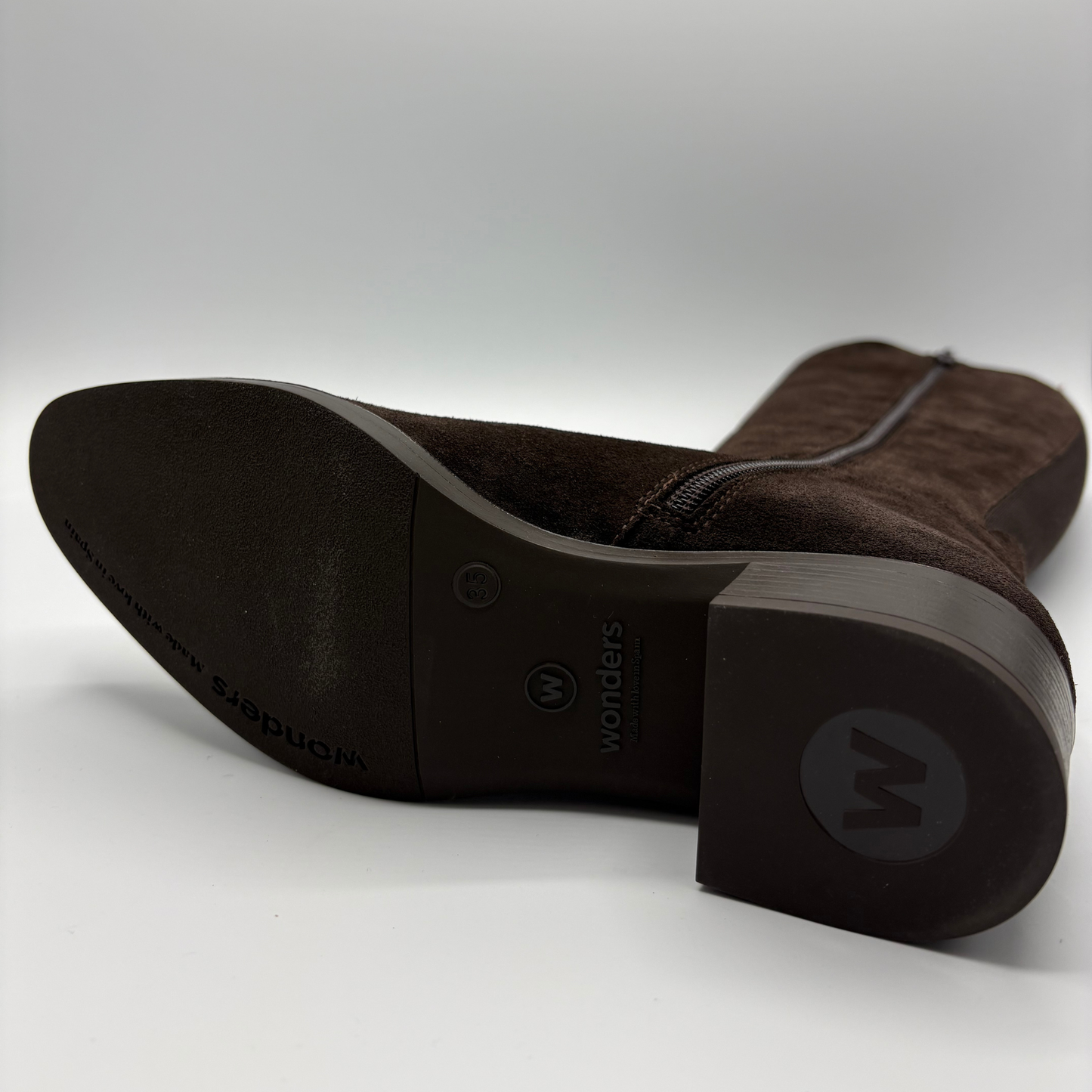 A close-up studio shot of the sole and heel of a dark brown suede boot. The brand name 'Wonders' is clearly embossed on the black outsole and printed on the heel cap.