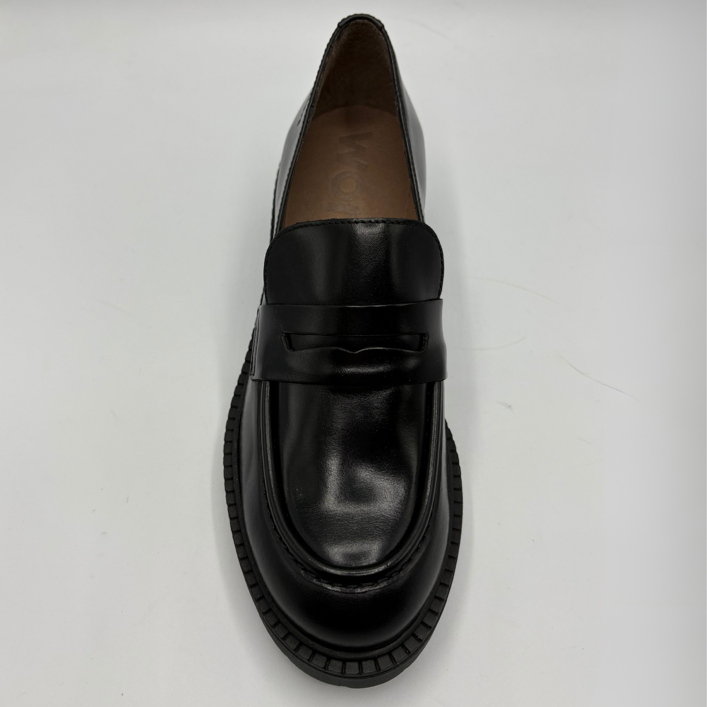 A single black leather penny loafer with a chunky black sole, photographed from a top-down angle on a light gray background.