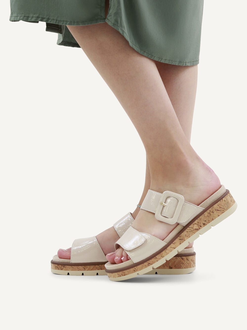 Beige sandals with cork sole worn by a person in a green skirt on a white background