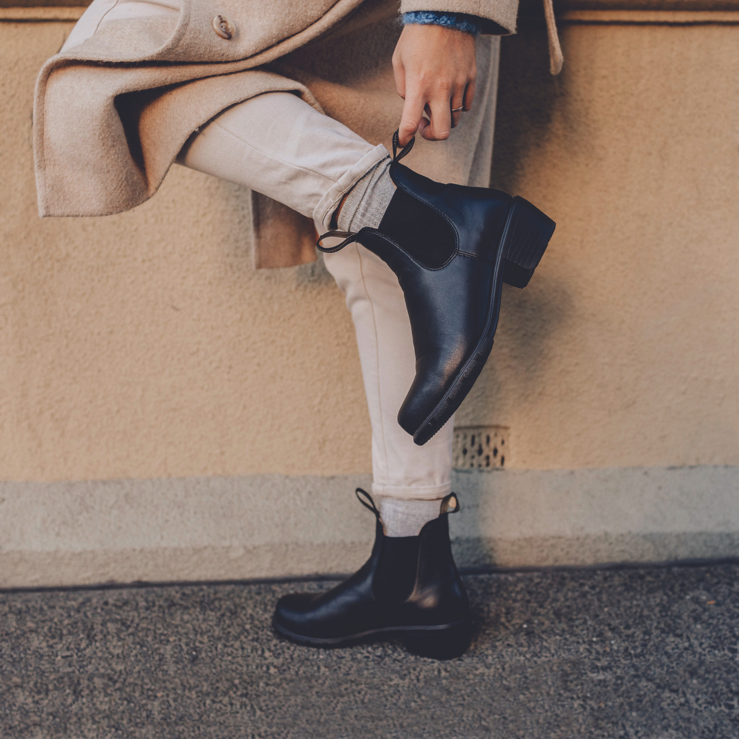 Person lifting one heel while wearing black, leather boots.
