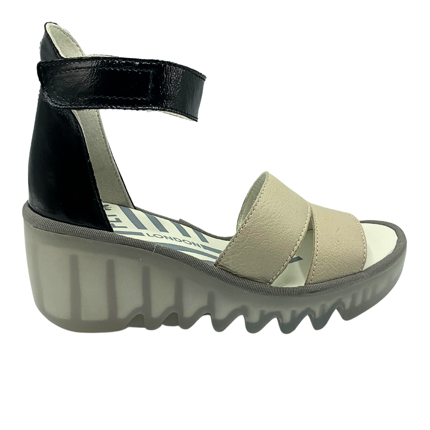 Outside view of a lower wedge Fly London sandal. Two-tonw with black heel cup and ankle strap and cream straps in front.