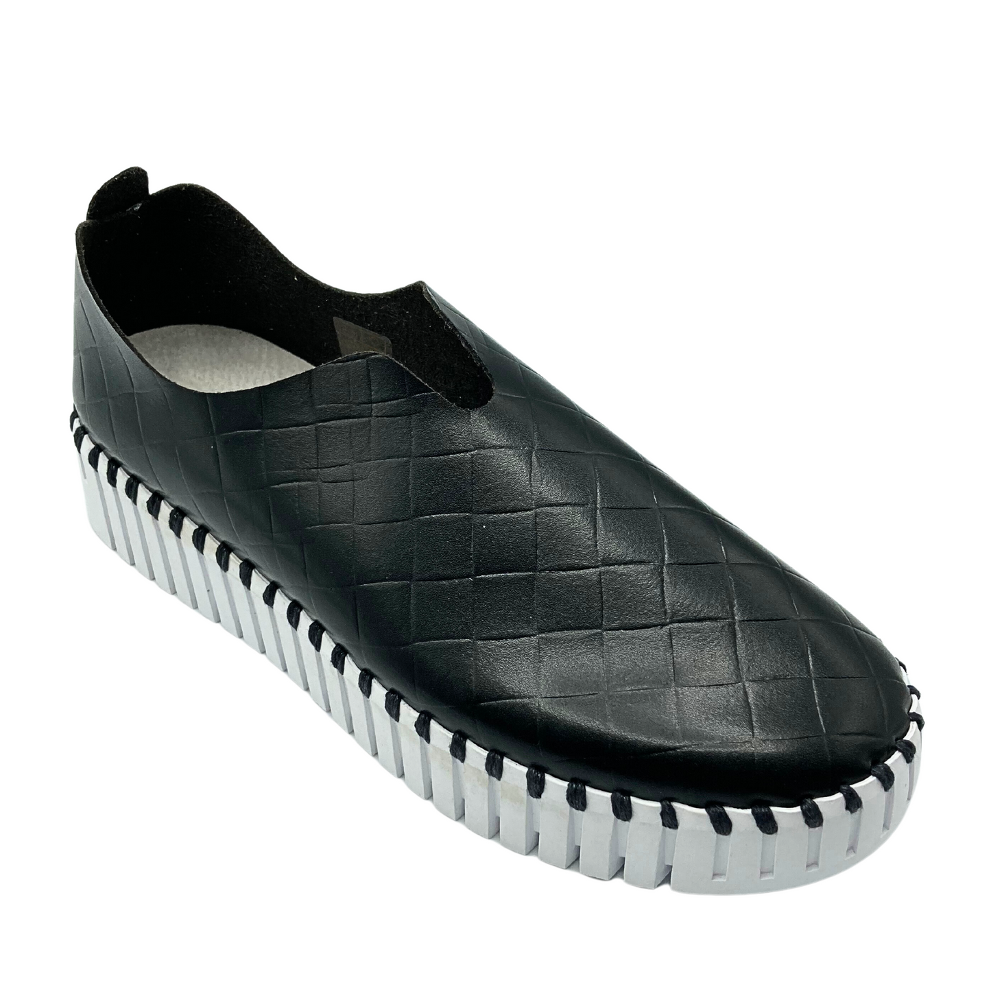 Angled side view of a slip on sneaker. Shown in black with a white sole and also available in white with a white sole.It is a man made material with a woven texture.