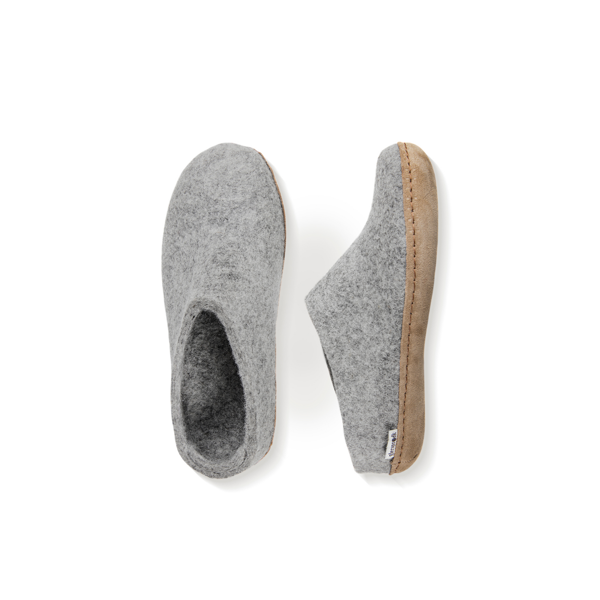An overhead view of two light grey felted wool slippers. One is pictured straight on, showing the top face of the slipper, while the other lays on its side, showing the profile with tan leather sole with a row of stitching.