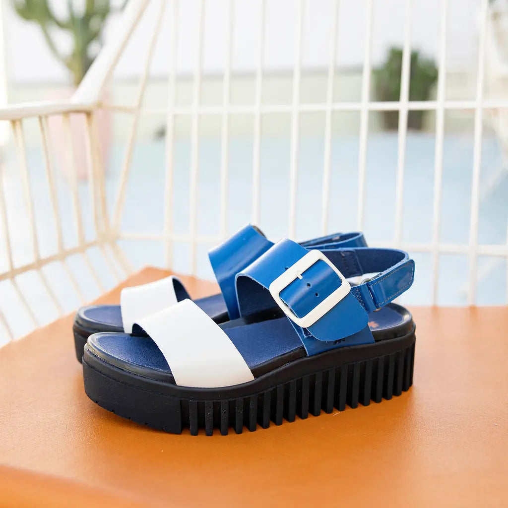 Blue and white sandals with a black sole on a wooden surface.