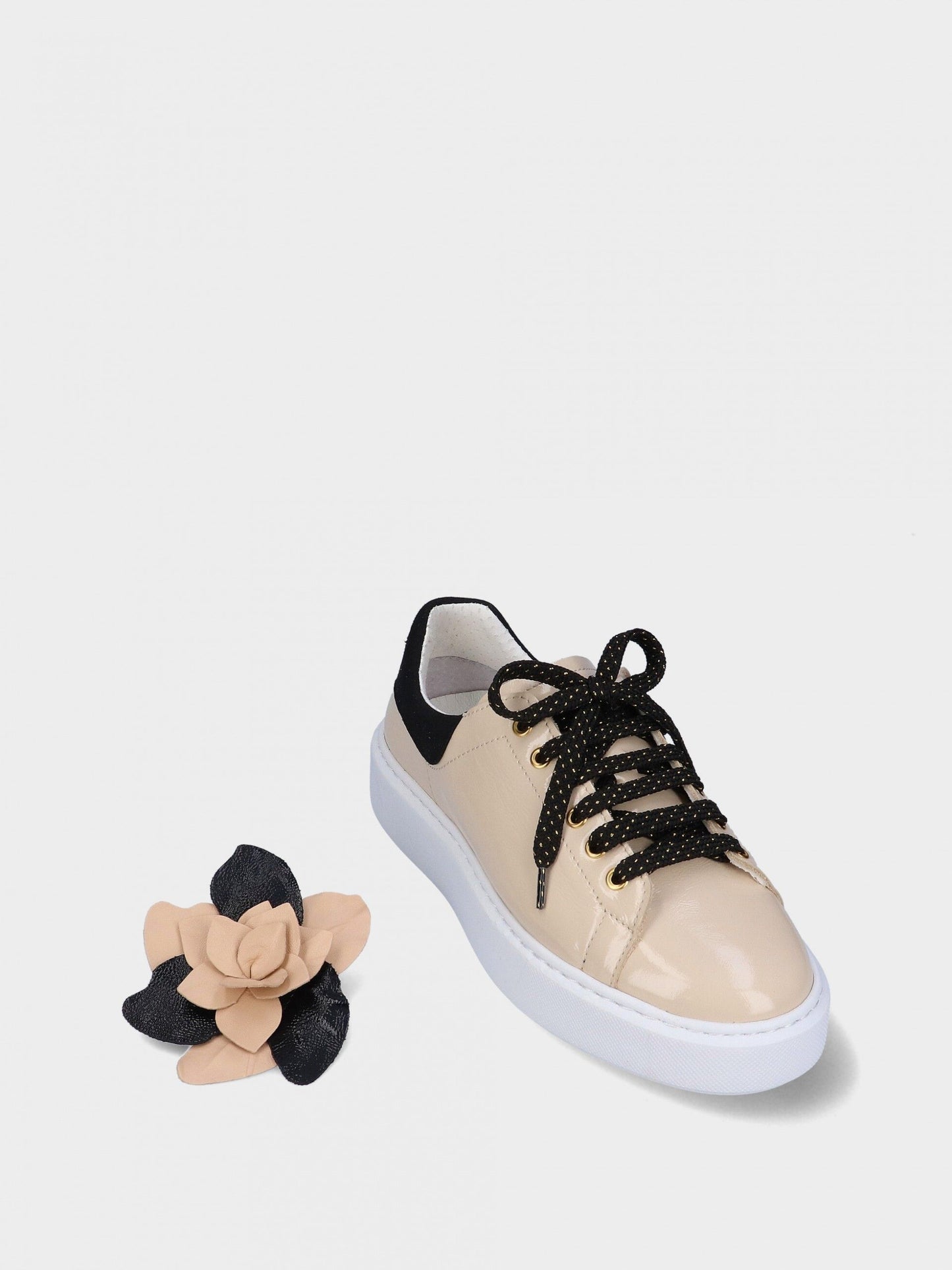 Beige sneaker with black laces and a removable floral accessory on a white background