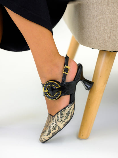 Black high-heeled shoes with gold accents worn by a person sitting on a chair.