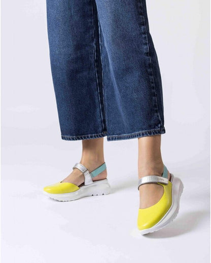 Yellow shoes with silver straps worn with blue jeans on a white background