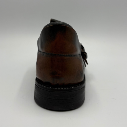 A close-up rear view of a dark brown leather loafer with a black sole, set against a plain light gray background.