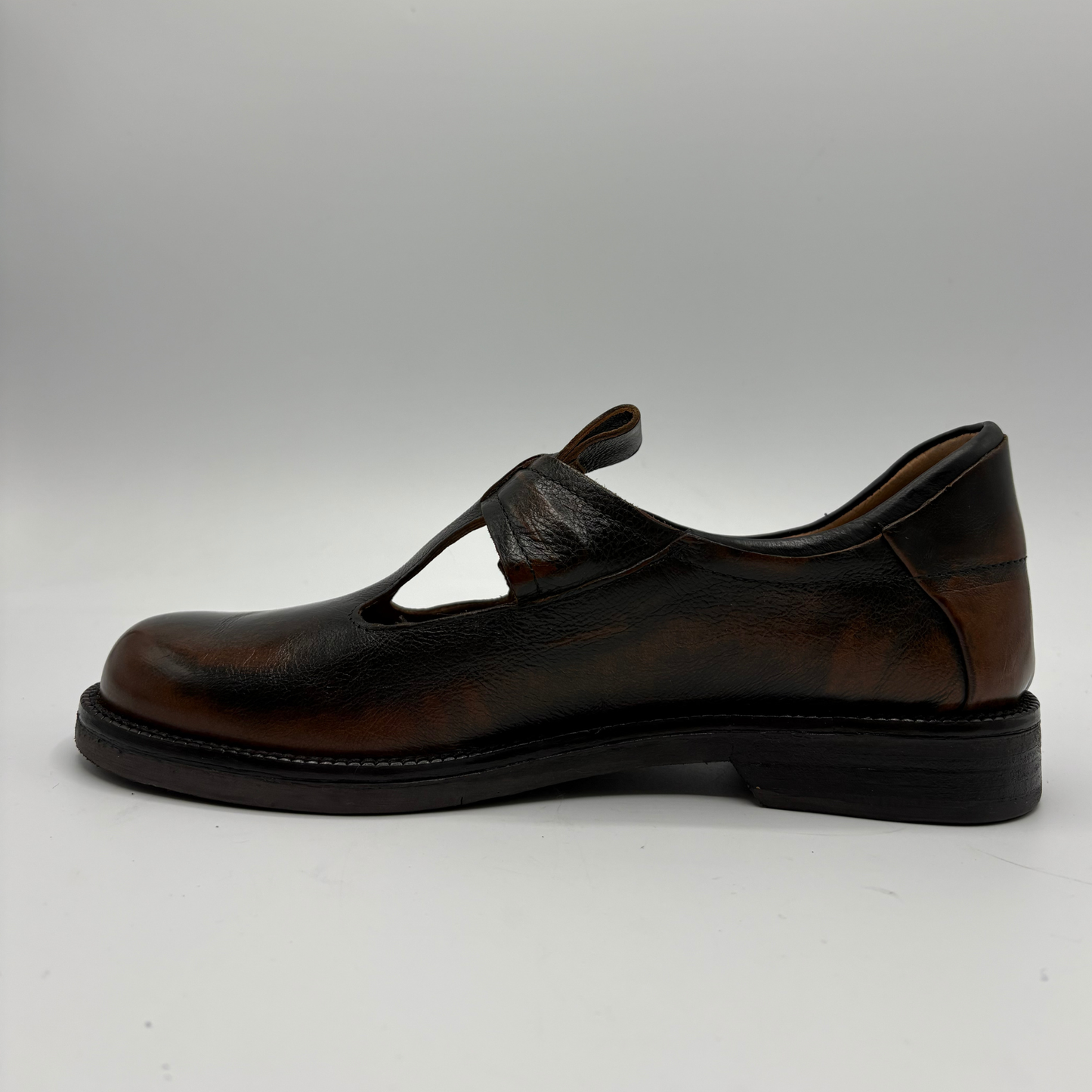 A single dark brown leather Mary Jane shoe with a cutout strap and low block heel, shown in profile against a neutral gray background.